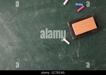 Gelöschte und schmutzige Klassenschultafel mit weißer und farbiger Kreide und Radiergummi auf der Oberseite. Draufsicht Stockfoto