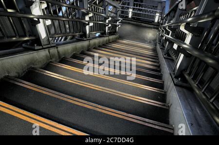 Blick hinunter eine dunkle Betontreppe mit zwei leuchtend gelben Warnstreifen am Rand jeder Treppe und Metallgeländer Stockfoto