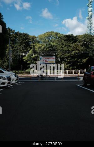 MATSUYAMA, JAPAN - 23. Sep 2019: Eine vertikale Aufnahme einer Person, die in der Nähe von Autos auf einem von Bäumen umgebenen Parkplatz Fahrrad fährt Stockfoto