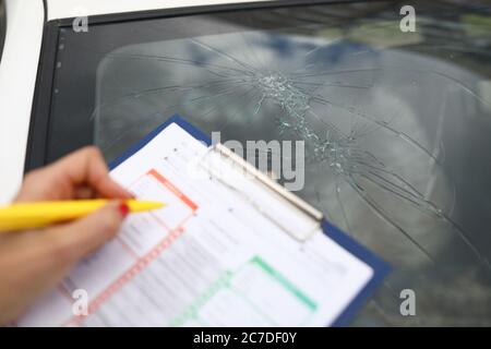 Ein Agent erstellt Dokumente für defekte Windschutzscheibe im Auto. Stockfoto