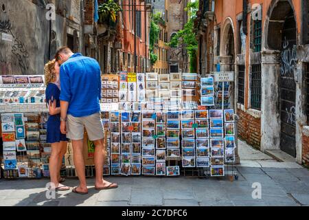 Das romantische Paar drückt seine Liebe aus, indem es im Zentrum von Venedig neben einem Postkartenladen küsst. Venedig, Italien. Römisches Paar, das sich bei Canal küsst Stockfoto