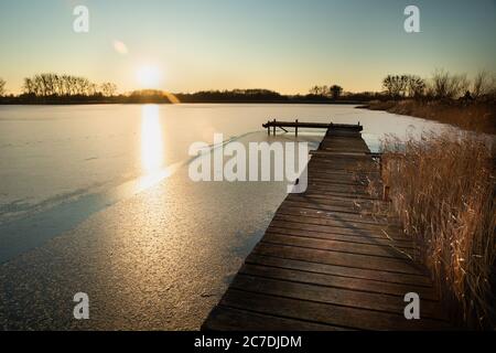 Eine hölzerne Plattform auf einem gefrorenen See und die Sonne über dem Horizont, sonniger Wintertag Stockfoto