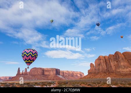 USA, Arizona, Monumnet Valley, Heißluftballons während des Balloon Festivals fliegen über Kamel Butte im Navajo Tribal Park. Die drei Schwestern sind links. Stockfoto