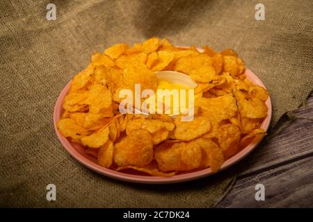 Kartoffelchips auf einer runden Platte und einem Topf mit Käsesauce. Nahaufnahme Stockfoto