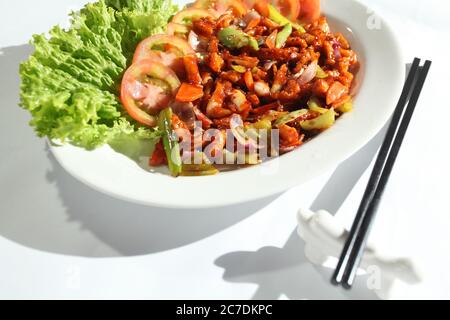High-Angle-Schuss einer Schüssel mit Salat und Tomaten In einem weißen Teller mit zwei schwarzen Essstäbchen Stockfoto
