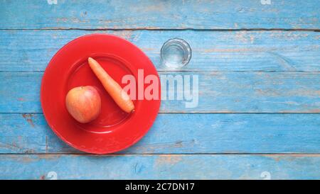 Apfel und Karotte auf einem roten Teller und ein Glas Wasser, Diät, gesunde Ernährung, Fitness-Konzept, flach legen Stockfoto