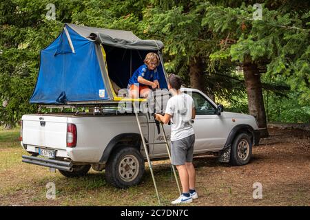 Authentische zwei junge Leute entladen Rucksack von Auto-Camping-Zelt auf dem Dach eines Nissan SUV in den Bergen Stockfoto