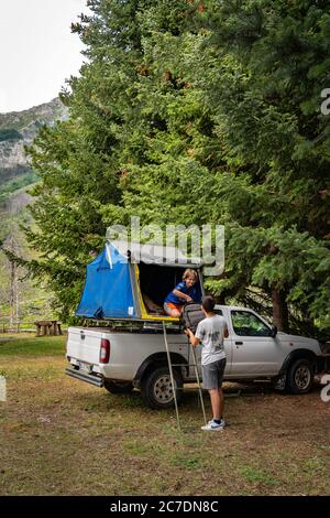 Authentische zwei junge Leute entladen Rucksack von Auto-Camping-Zelt auf dem Dach eines Nissan SUV in den Bergen Stockfoto