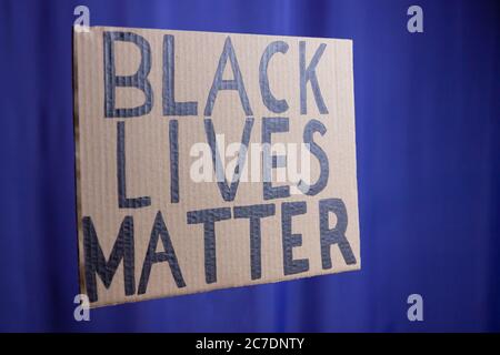SCHWARZ LEBT MATERIE auf einem blau verschwommenen Hintergrund. Kein Rassismus-Konzept. Karton-Banner mit dem Text "Black Lives Matter". Konzept des Kampfes um die sparsam Stockfoto