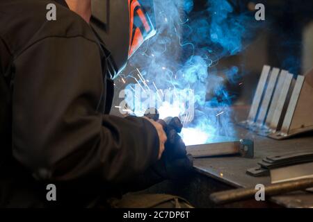 Unanstiraler Arbeiter in Maske, beim Schweißen von Metall mit hellem Licht, Rauch und Funken Stockfoto