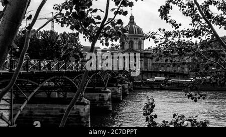 Graustufenaufnahme der Fußgängerbrücke Pont des Arts in der Nähe des Instituts De France umgeben von Bäumen Stockfoto