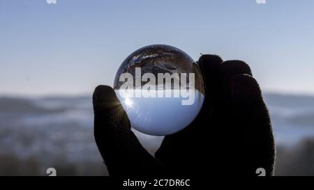 Nahaufnahme einer Hand in einem schwarzen Handschuh halten Eine Glaskugel, die den Boden darunter reflektiert Stockfoto