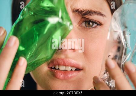 Close up Mädchen Abdeckung Gesicht mit leeren Plastikflaschen, während leider in der Kamera über bunten Hintergrund Stockfoto