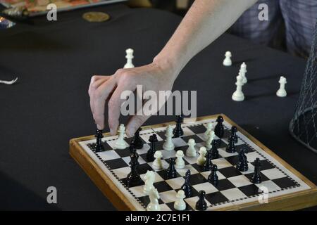 Schachspiel. Hand eines jungen Mannes, der Schachfiguren auf einem Brett mit weißen und schwarzen Figuren auf schwarzem Hintergrund bewegt. Stockfoto