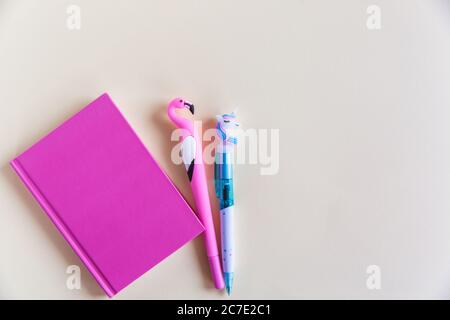 Pinkes Notizbuch für Notizen, lustige Einhorn- und Flamingostifte auf gelbem pastellfarbenem Hintergrund. Flach liegend. Draufsicht. Speicherplatz kopieren Stockfoto