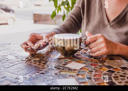Frau Hände halten eine Tasse Cappuccino Kaffee auf einem farbigen Glastisch im Café Stockfoto