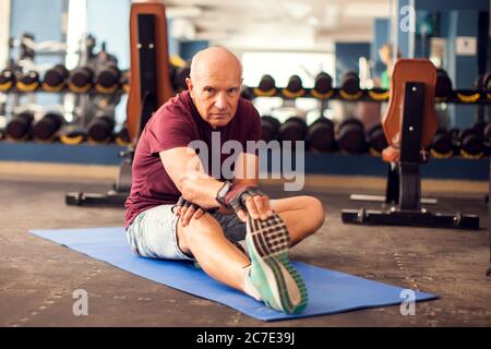 Ein Porträt von kahlen älteren Mann beim Stretching nach dem Training in der Turnhalle. Menschen, Gesundheit und Lifestyle-Konzept Stockfoto