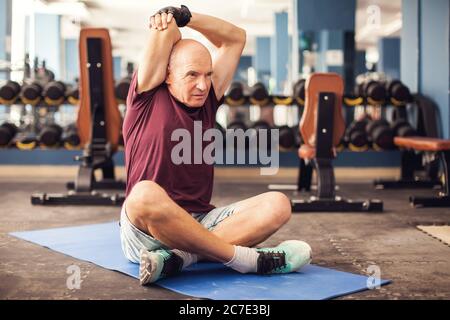Ein Porträt von kahlen älteren Mann beim Stretching nach dem Training in der Turnhalle. Menschen, Gesundheit und Lifestyle-Konzept Stockfoto
