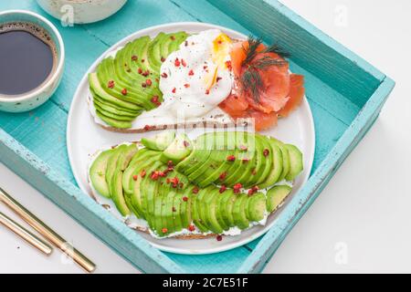 Bruschetta mit gesalzenem Lachs, gehackter Avocado, Pfeffer und pochiertem Ei auf einem weißen Teller auf türkisfarbenem Hintergrund Stockfoto