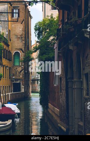 Vertikale Aufnahme eines schmalen Kanals mit Booten auf der Seite in Venedig, Italien geparkt Stockfoto