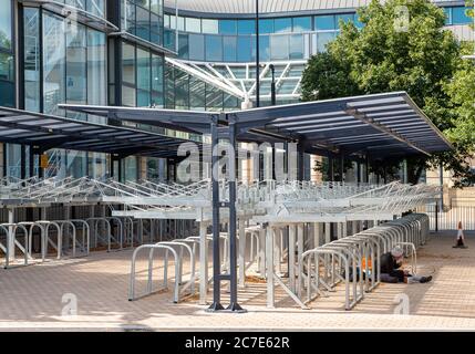 Maidenhead, Berkshire, Großbritannien. Juli 2020. Ein Obdachloser sitzt gegen leere Fahrradständer am Bahnhof Maidenhead, da die Zahl der Pendler nach der Coronavirus Covid-19 Pandemie Sperre deutlich unter den üblichen Zahlen bleibt. Quelle: Maureen McLean/Alamy Stockfoto