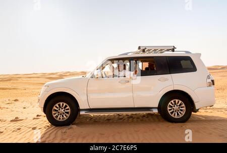 Wahiba Sands, Oman - 12. Februar 2020: Glücklicher Omani in traditionellem Gewand fährt den weißen Offroad 4x4 mit Touristen an Bord in der Wahiba Sa Stockfoto