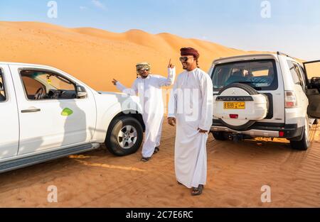 Wahiba Sands, Oman - 12. Februar 2020: Fröhliche omanische Männer in traditioneller Kleidung haben Spaß mit weißen 4x4 Offroad Autos in Wahiba Sands Desert, Sultanat Stockfoto