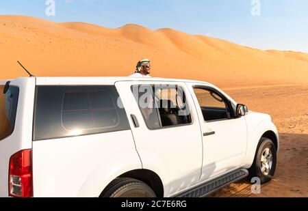 Wahiba Sands, Oman - 12. Februar 2020: Der weiße Geländewagen mit Omani in traditioneller Kleidung in der Wahiba Sands Wüste, Sultanat Oman. Stockfoto