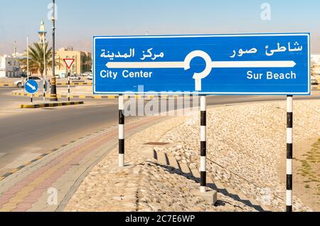 Straßenschild mit Hinweis auf das Stadtzentrum und den Strand an der Straße in Sur, Sultanat von Oman. Stockfoto