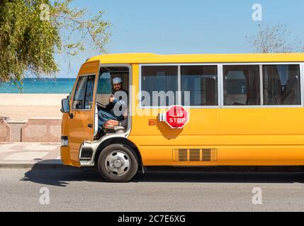 Sur, Oman - 15. Februar 2020: Gelber Bus mit Fahrer in traditioneller omanischer Kleidung Blick auf CAM, auf der Straße von Sur, Sultanat von Oman, Naher Osten Stockfoto