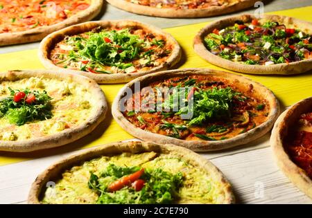Verschiedene Pizzabücken für die Speisekarte. Pizza mit Fleisch, grünen Zwiebeln, Tomaten und Salat auf Holzgrund. Nehmen Sie Lebensmittel mit verschiedenen Zutaten und knackigen Kanten. Italienische Pizza und Pizzeria Konzept Stockfoto