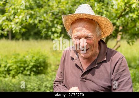 Porträt eines lächelnden älteren Mannes mit Hut im Garten seines Gemüsegartens im Frühling. Stockfoto