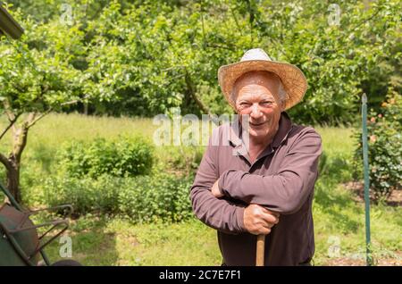 Porträt eines lächelnden älteren Mannes mit Hut im Garten seines Gemüsegartens im Frühling. Stockfoto