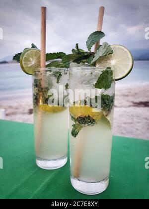 Nahaufnahme von zwei Mojitos in hohen Gläsern mit hölzernen Strohhalmen auf einem grünen Tisch an einem Strand in Indonesien Stockfoto