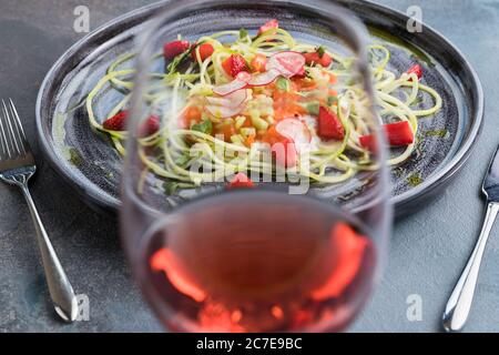 Lachskartare mit frischen Erdbeeren und Zucchini-Spaghetti. Rustikaler Holzhintergrund, graue Tischdecke und ein Glas Rotwein. Draufsicht Stockfoto