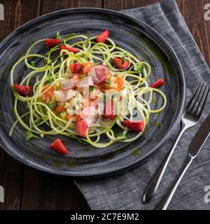 Lachskartare mit frischen Erdbeeren und Zucchini-Spaghetti. Rustikaler Holzhintergrund, graue Tischdecke. Draufsicht Stockfoto