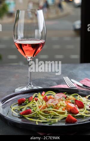 Lachskartare mit frischen Erdbeeren und Zucchini-Spaghetti. Rustikaler Holzhintergrund, graue Tischdecke und ein Glas Rotwein. Draufsicht Stockfoto