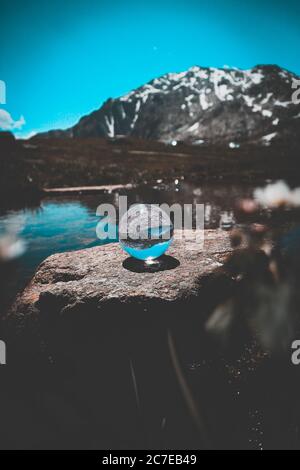 Eine Glaskugel auf Felsformation in der Nähe eines Sees mit Die Spiegelung der felsigen Berge und der blaue Himmel Stockfoto