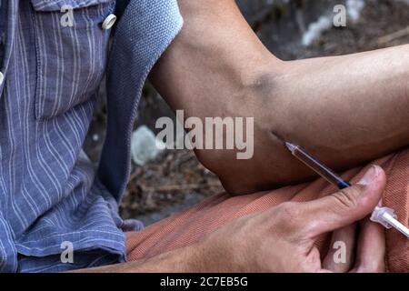 Hände eines Drogenabhängigen mit einer Spritze voll Betäubungsmittel, Heroin oder Kokain in die Armvenen. Drogenabhängigkeit und Entzugserscheinung. Stockfoto