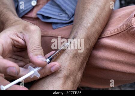 Hände eines Drogenabhängigen mit einer Spritze voll Betäubungsmittel, Heroin oder Kokain in die Armvenen. Drogenabhängigkeit und Entzugserscheinung. Stockfoto