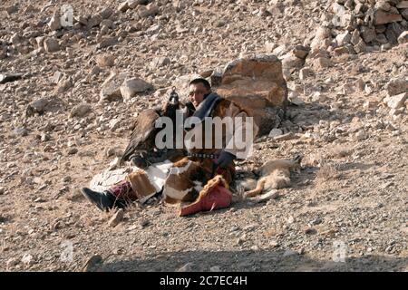 Ein kasachische Nomade, der mit seinem Steinadler ruhte, nachdem er einen Fuchs im Altai-Gebirge der westlichen Mongolei gefangen hatte. Stockfoto