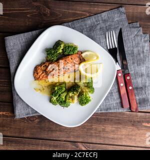 Gegrilltes Forellensteak auf einem weißen Teller mit Brokkoli und Limette. Besteck auf dem Holzhintergrund Stockfoto