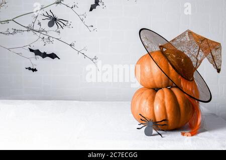 Kürbisse mit Hexenhut und einer Papierspinne DIY auf weißem Hintergrund mit einem Brunch mit Fledermäusen. Minimale Halloween-Karte Stockfoto