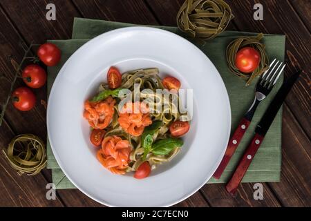 Tagliatelle itakian traditionelle Pasta mit Forelle aus nächster Nähe auf einem weißen Teller. Besteck und Tomaten auf dem Holzhintergrund Stockfoto