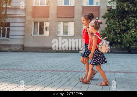 Glückliche Schwestern Mädchen tragen Rucksäcke gehen zur Schule halten Hände. Bildung Stockfoto