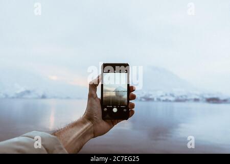 Eine Person mit einem Smartphone, die ein Bild von schön Berge in der Nähe des Sees umgeben von Nebel Stockfoto