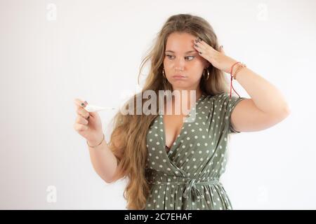 Ziemlich blonde Mädchen in einem grünen Kleid suchen den Test mit der Geste der Sorge Stockfoto