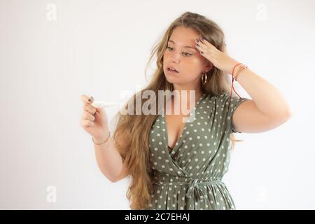 Ziemlich blonde Mädchen in einem grünen Kleid suchen den Test mit der Geste der Sorge Stockfoto