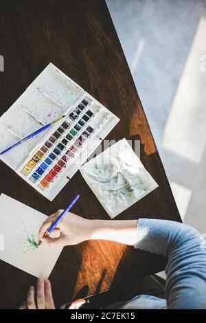 Overhead-Aufnahme einer Person, die mit Aquarellen und einer weißen Aquarellpalette malt. Stockfoto