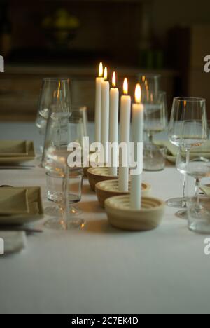 Vertikale Aufnahme von fünf brennenden weißen Kerzen auf einem Tisch Mit Weingläsern und Besteck Stockfoto